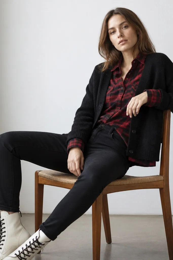 A black cardigan worn open over a red-and-black plaid flannel shirt. The flannel collar shows above the cardigan neckline. Black jeans and white lace-up boots finish the look.