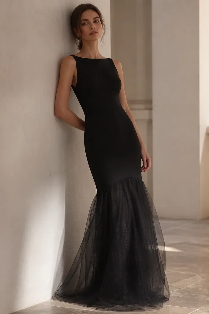 A black column dress with a matte black base layer and a sheer tulle overlay along the skirt. The overlay forms soft volume near the lower half, with a smooth top section.