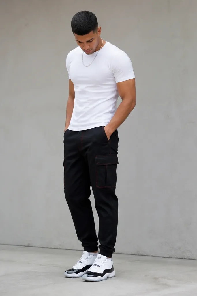Photo showing black cargo pants with subtle red stitching details, a white fitted tee, and white/black Jordan 11 sneakers with patent leather parts. The pants have a taper and the hem sits above the shoe.