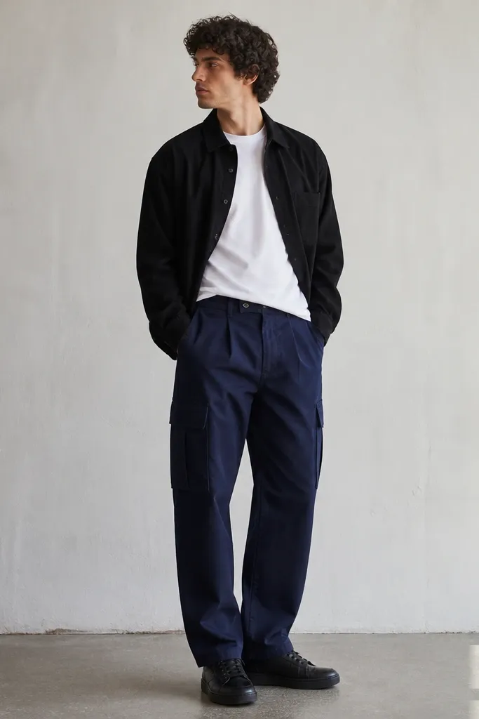 Indigo blue cargo pants with a white heavyweight t-shirt tucked slightly in front and a black overshirt layered on top. The outfit is finished with black leather sneakers.