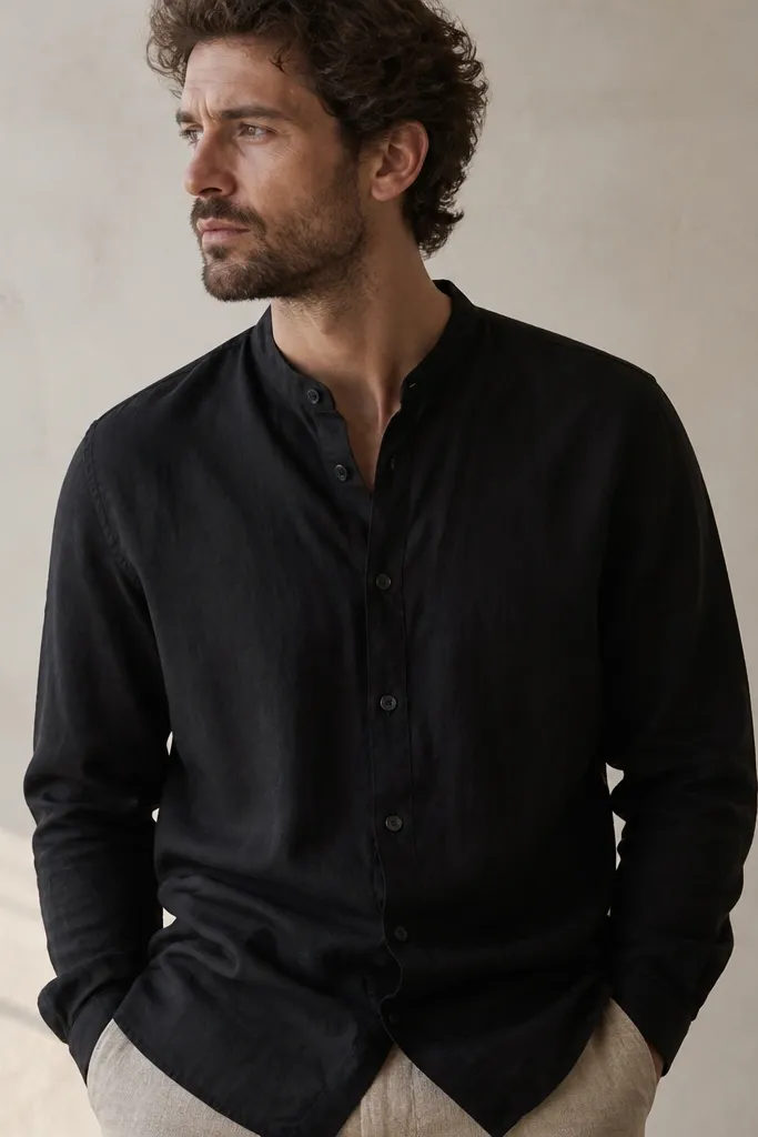A black linen shirt with a short mandarin collar. The fabric shows a slight grain and the buttons are dark and matte. The shirt is photographed with relaxed folds around the torso.