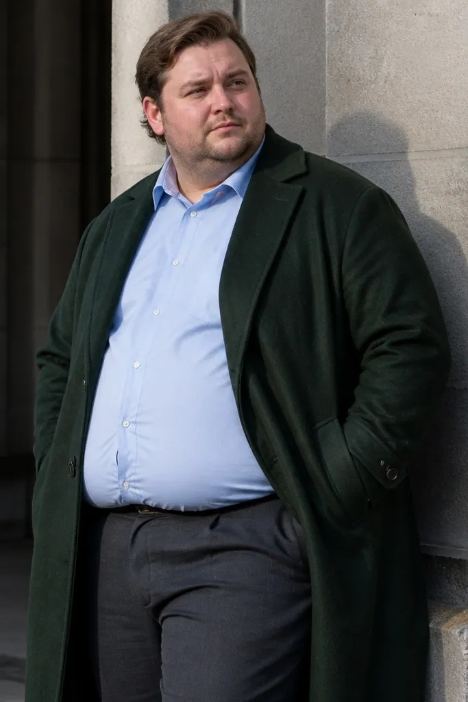 Deep green overcoat over a light blue shirt with charcoal trousers and black leather shoes