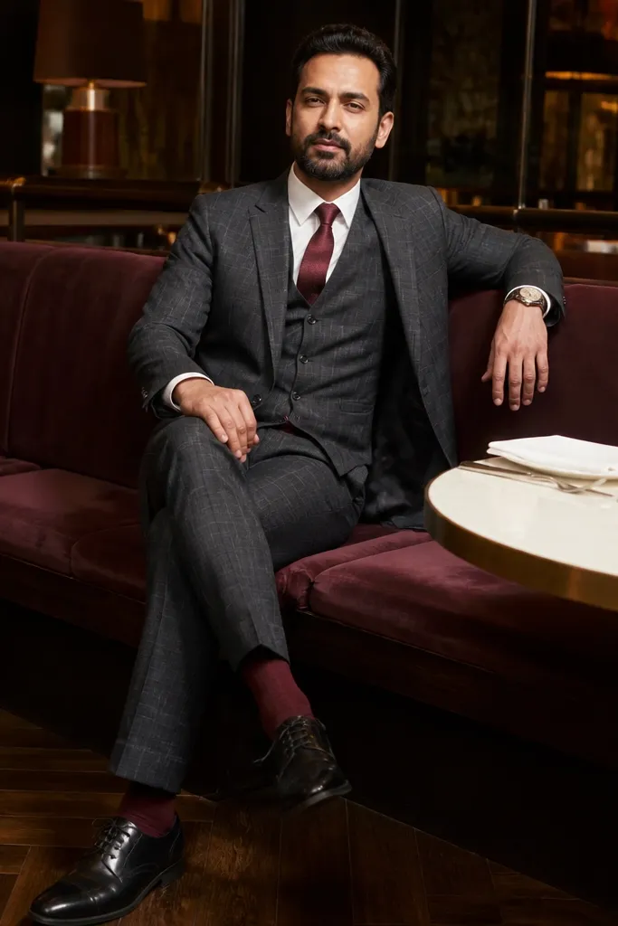 Grey check three-piece suit with burgundy tie, white shirt, and burgundy socks with black shoes